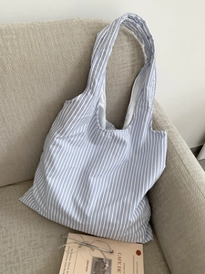 Gros plan d'un sac cabas en toile rayé bleu et blanc posé sur un canapé avec décor