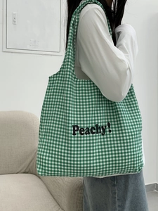 Detail of green plaid canvas tote bag with Peachy text print on shoulder
