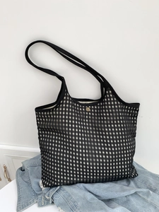 Detail of checkered canvas tote bag with golden clasp resting on denim jacket