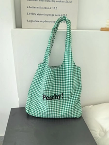 Detailed shot of green checkered nylon tote bag with Peachy letter print on casual display