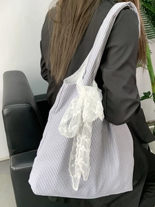 Detail of blue striped canvas tote bag featuring a large white lace bow for casual use