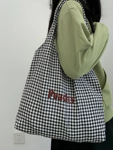 Side view of black and white plaid canvas tote bag with red Peachy text on a model