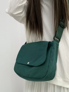 Detail of dark green canvas messenger bag featuring a round metal buckle and wide strap