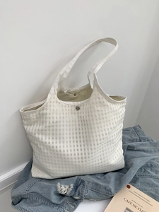Detail of white checkered tote bag featuring mesh texture and secure metal snap closure