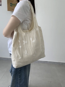 Detailed embroidery of leaf patterns on a cream canvas tote bag for summer