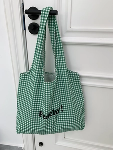 Detail of green and white checkered canvas tote bag with black Peachy! text on door handle