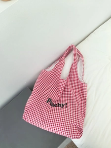 Close-up of red gingham tote bag featuring bold Peachy! print in a clean home setting