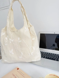 Detailed embroidery of white leaves on a creamy lace tote bag next to a laptop