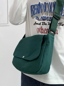Detail of dark green canvas messenger bag with silver metal button and adjustable strap