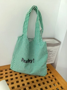 Detail of green and white checkered canvas tote bag with black Peachy text on a wooden bench