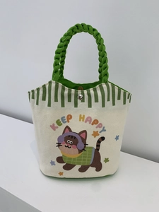 Detail of canvas tote bag showing green woven handles and cute cartoon cat print