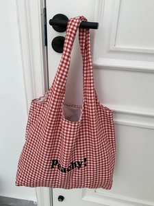 Detail of red gingham canvas tote bag featuring Peachy print hanging on a white door