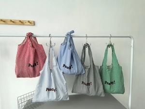 Detail of diverse striped and checkered nylon tote bags with Peachy lettering on hooks