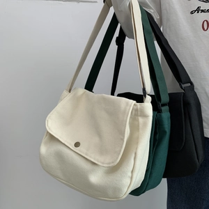 Close-up of canvas messenger bags in beige, green, and black with metal magnetic buckles