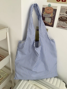 Détail d'un sac cabas en toile à rayures bleues et blanches suspendu dans un décor épuré