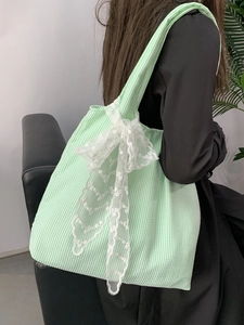 Detail view of a green striped canvas tote bag with a large white lace bow accent