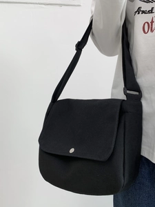 Detail of black canvas messenger bag featuring a silver metal snap button and strap