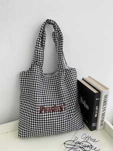 Detail of checkered canvas tote bag with red Peachy text hanging on a clean white wall