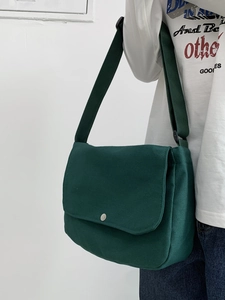 Detail of dark green canvas messenger bag with metal buckle on white background