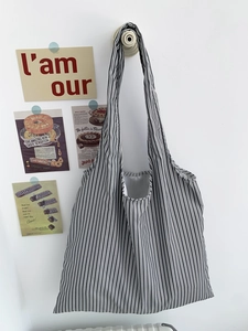 Grand sac fourre-tout rayé avec larges bandoulières accroché sur un mur blanc