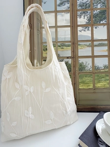 Detailed close-up of intricate white leaf embroidery on a cream lace tote bag