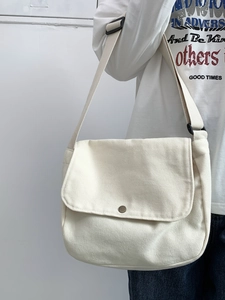 Detail of off-white canvas messenger bag featuring metal button closure and adjustable strap