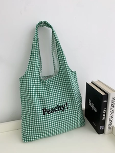 Detail of green and white plaid canvas tote bag with black Peachy! print and books