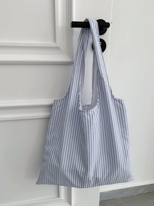Détail du sac cabas à rayures bleues et blanches avec bandoulières suspendu à une porte