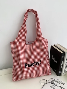 Detail of red checkered canvas tote bag with Peachy! text hung on a white wall
