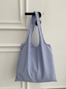 Détail d'un sac cabas en toile à rayures bleues et blanches accroché à une poignée de porte
