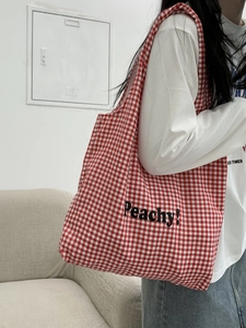 Detail of red gingham canvas tote bag with Peachy! print shown on shoulder