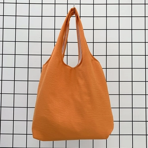 Detail of a bright orange canvas tote bag with wide shoulder straps on a grid background