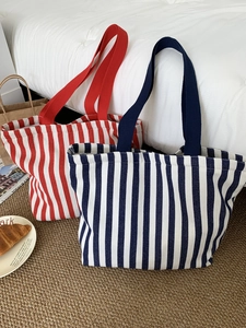 Detail view of large canvas tote bags in red and dark blue stripes on a soft carpet