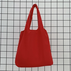Detail of red canvas tote bag hanging on a grid background showing durable fabric texture