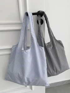 Détail de sacs à bandoulière en toile rayée suspendus à une poignée de porte blanche