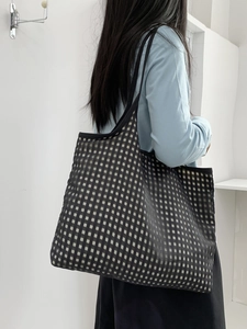 Rear view of a large black and white checkerboard tote bag worn by a model