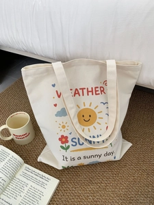 Dettaglio borsa tote in tela crema con stampa sole e arcobaleno su tappeto marrone