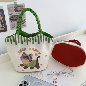 Detail of canvas bucket bag with cute cat illustration and green woven handles on desk