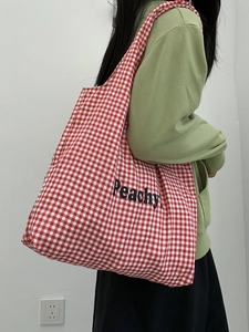 Detail of red and white checkered canvas tote bag with Peachy lettering on shoulder