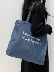 Detail of embroidered 'Less Mondays More Sundays' slogan on blue denim tote bag