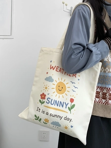 Dettaglio della borsa tote in tela con stampe di cartoni animati, sole e fiori color crema