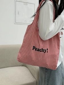 Detail of red gingham canvas tote bag with Peachy slogan shown on a shoulder
