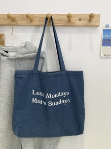 Detail of blue denim tote bag featuring white Less Mondays More Sundays embroidery