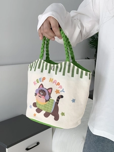 Close-up of canvas bucket bag featuring cartoon cat print and green woven handles