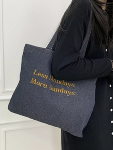 Detailed close-up of dark blue denim tote bag with Less Mondays More Sundays gold embroidery