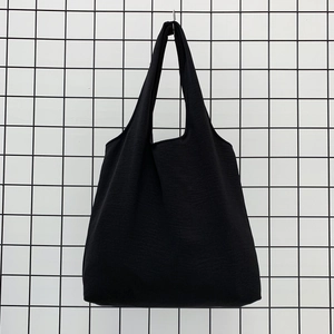 Detail of a minimalist black canvas tote bag with wide shoulder straps on a grid display