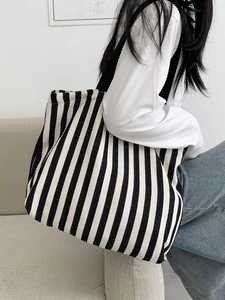 Side view of a large black and white striped canvas tote bag worn by a model in a room