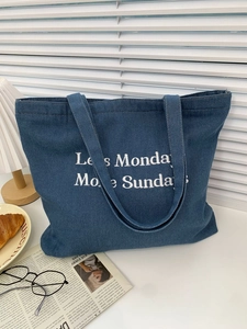 Detail of large denim tote bag with white 'Less Monday More Sunday' slogan embroidery