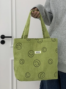 Detail of green corduroy tote bag with smile patterns and brand label in hand