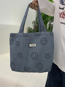 Detailed texture of blue corduroy tote bag featuring black smile patterns and white label